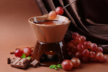 Chocolate fondue with fruits, on  brown background