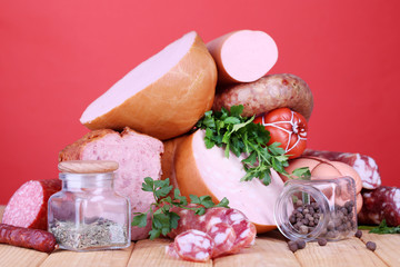 Lot of different sausages on wooden table on red background