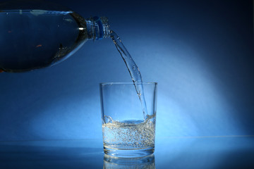 Pour water from bottle into  glass, on dark blue background