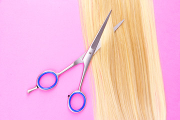 Long blond hair with scissors on pink background