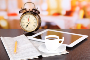 Tablet, newspaper, cup of coffee and alarm clock on wooden