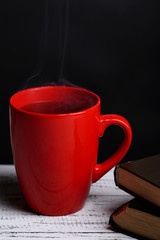 Cup of hot tea with books on table on dark background