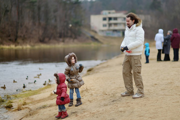 Obraz premium Father and daughters feeding ducks at autumn
