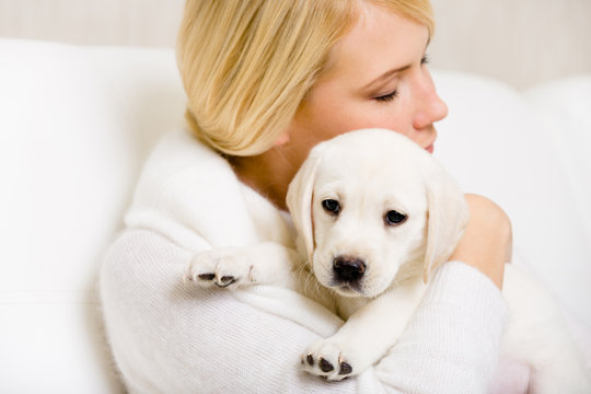 Woman in white sweater embraces Labrador puppy