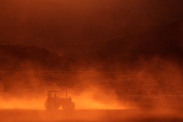 Tractor working in the field at sunset with dust