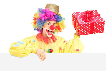 Obraz na płótnie Canvas Male clown with cheerful expression holding present behind blank