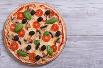 Mushroom pizza with olives, tomatoes and basil on the table
