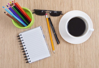 Notebook, cup of coffee and colorful pencils on wooden table