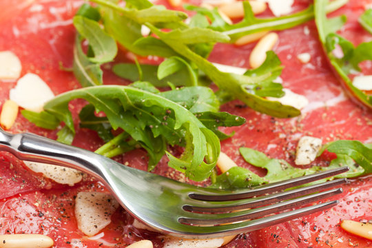Carpaccio auf einem Teller mit Parmesan und Pinienkernen