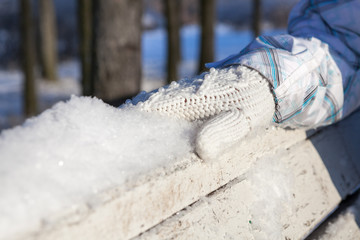 White knitted mitten on back of the bench in snow
