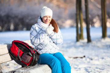 Fototapeta na wymiar Young woman with backpack heating hands in mittens, copyspace
