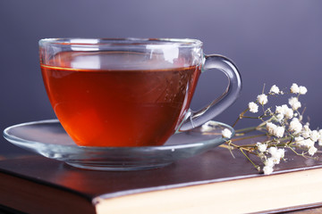 Cup of hot tea on book with flowers on table on gray background
