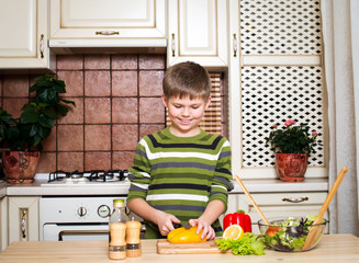 Smiling boy preparing a vegetable salad in the kitchen.