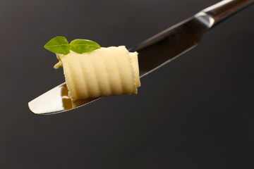 Curl of fresh butter with basil on knife on grey background