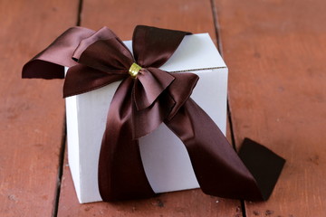 white gift box with ribbon bow on a wooden background