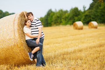 Naklejka na ściany i meble Young couple in love on yellow hay field on summer evening.