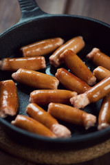 Fried oily mini sausages in a cast-iron pan, close-up