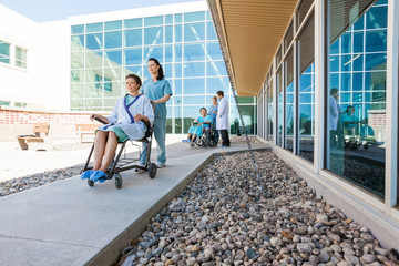 Medical Team With Patients On Wheelchairs At Hospital Courtyard
