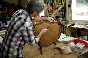 Craftsman repairing antique armchair in workshop