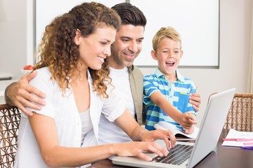 Laughing little boy using laptop with parents at table