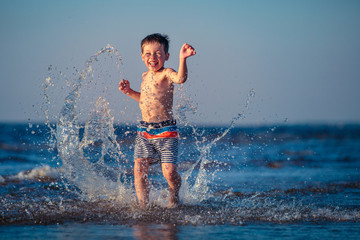 Fototapeta premium Little boy running through the water at beach