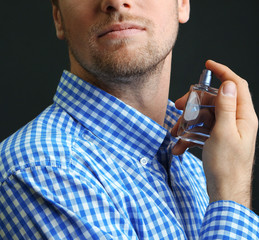Handsome young man using perfume on black background
