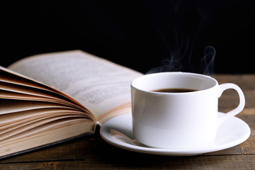 Cup of hot coffee with book on table on dark background