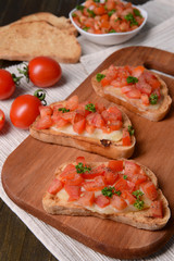 Delicious bruschetta with tomatoes on cutting board close-up