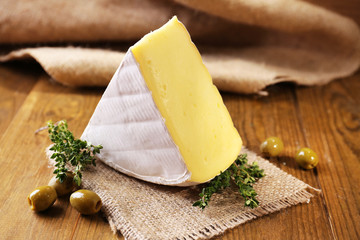 Tasty Camembert cheese with thyme and olives, on wooden table