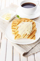 Grilled bread with butter and cup of coffee on wooden table