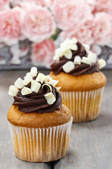 Fancy chocolate cupcakes on wooden table. Pink carnation flowers