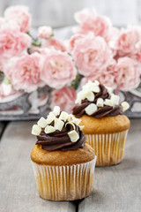 Fancy chocolate cupcakes on wooden table. Pink carnation flowers