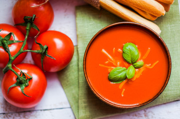 Tomatoe soup with bread sticks and basil on wooden background