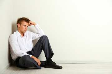 Young businessman  sitting on floor, on gray wall background