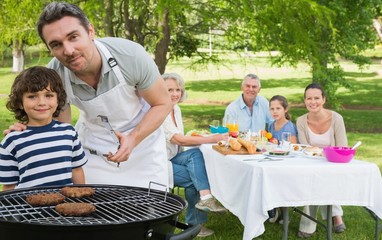 Father and son at barbecue grill with family having lunch in