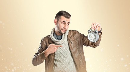Young businessman holding an antique clock over ocher background