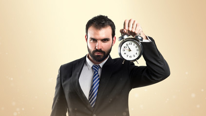 Young businessman holding an antique clock over ocher background