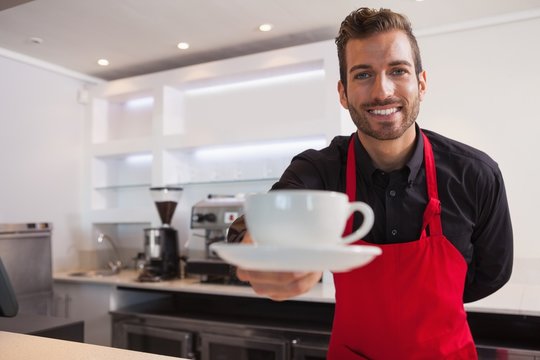 Happy barista offering cup of coffee to camera