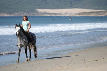 Blondes Mädchen auf Apfelschimmel am Strand