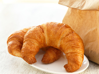 Two croissants on a plate and a paper bag
