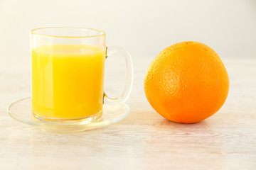 An orange next to a mug with juice