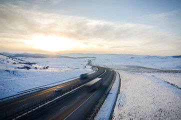 Highway road over the mountains with speeding cars and trucks on