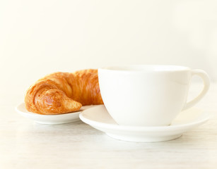 A little white coffee cup and a croissant