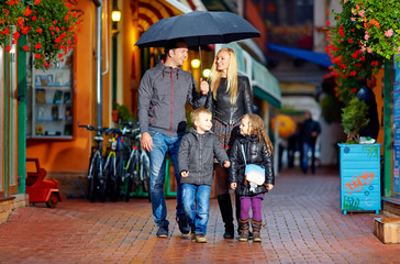 Obraz premium happy family walking under the rain on cozy colorful street