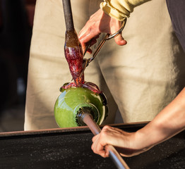 Glass blower works on ornate green bottle