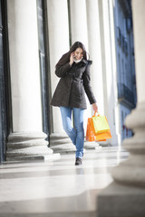 young woman with bags doing shopping in city and calling a frien