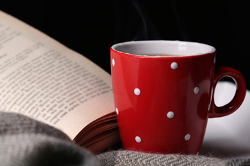 Cup of hot tea with book and plaid on table on dark background