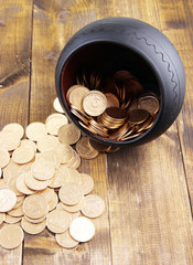 Golden coins falling out from pot, on wooden background