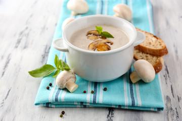 Mushroom soup in white pot, on napkin,  on wooden background