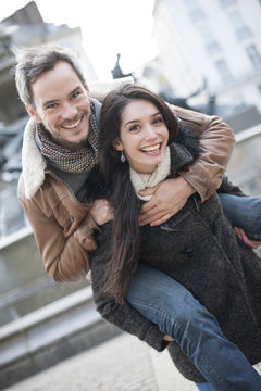 Cheerful young woman carrying boyfriend on his back